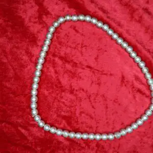 Silver beaded necklace arranged on red fabric.
