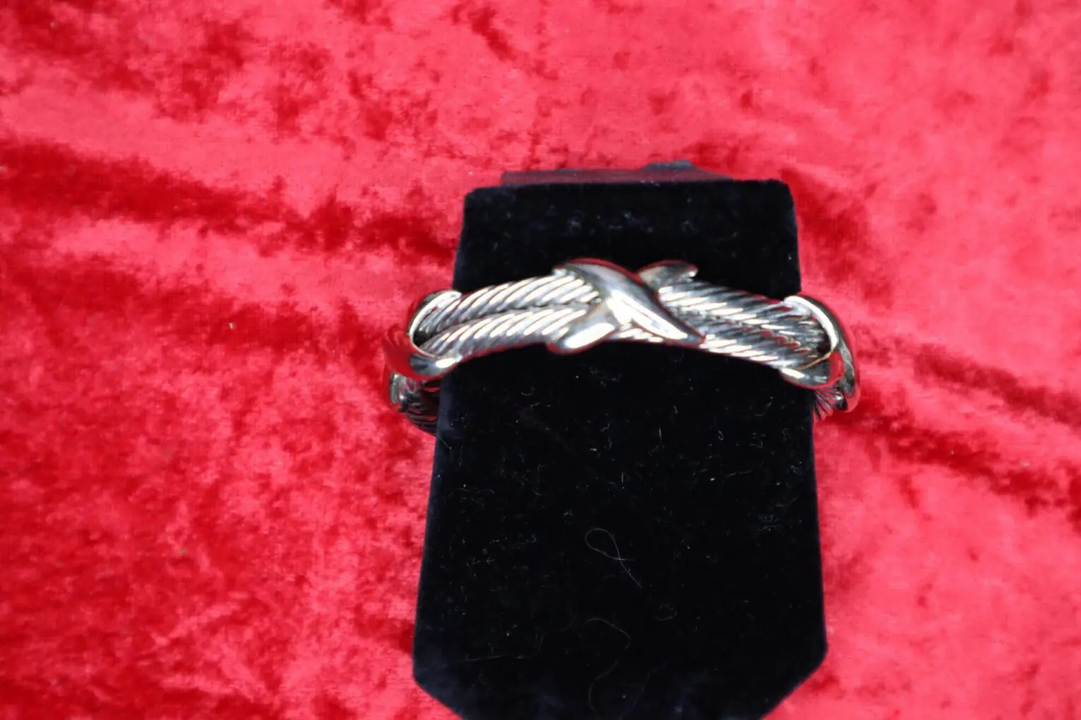 Silver twisted bracelet displayed on a black stand.