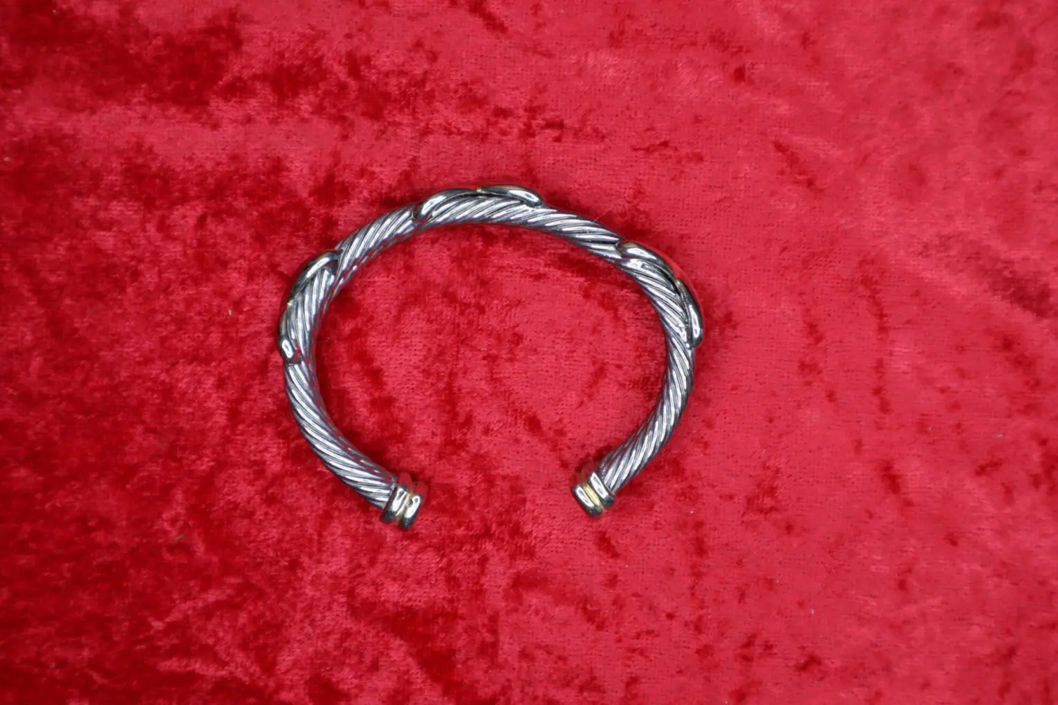 Twisted silver bracelet displayed on red fabric.