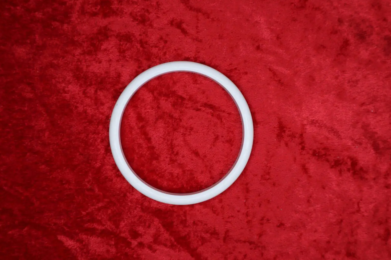 White circular bracelet on red velvet background.