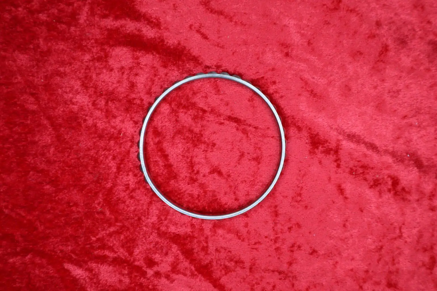 Silver hoop bracelet resting on red fabric.