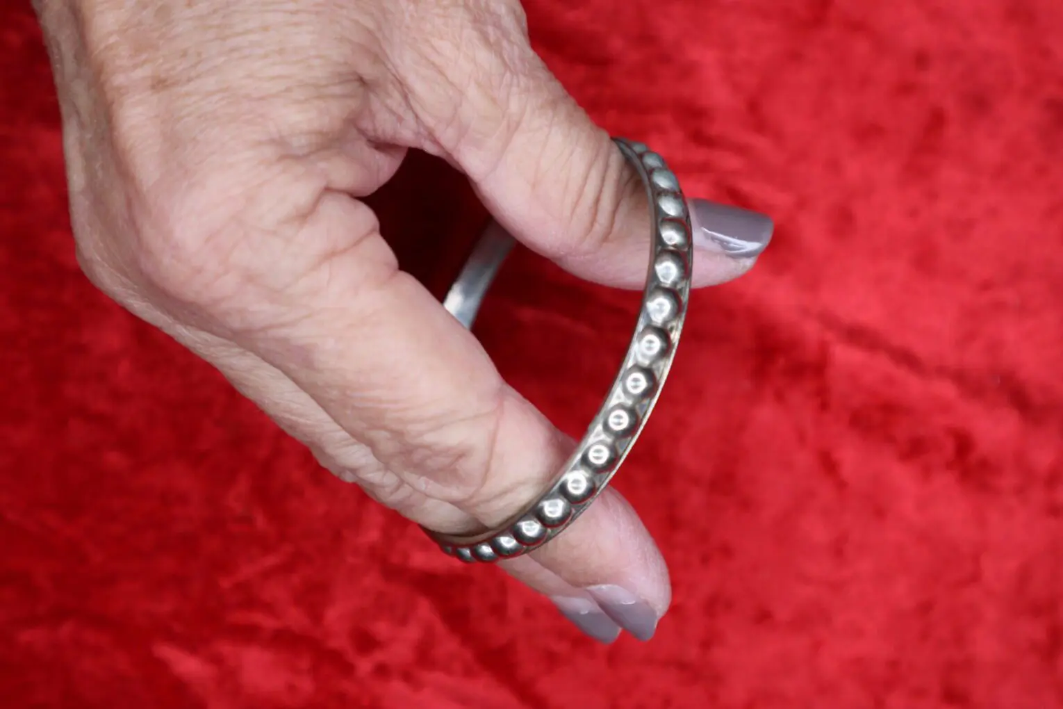 Silver bangle bracelet held against red fabric.