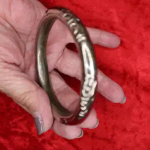Decorative silver bangle held against red background.