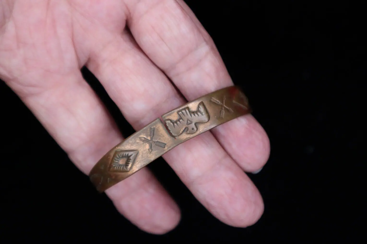 Bronze bracelet with engraved designs in hand.