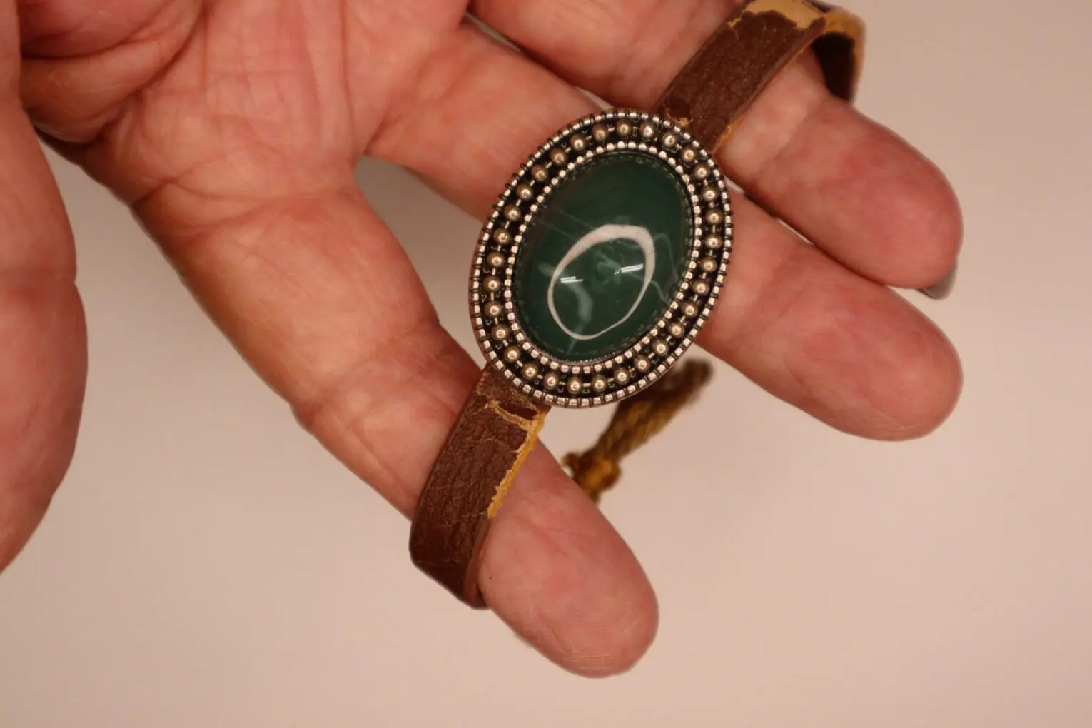 Brown leather bracelet with green stone centerpiece.