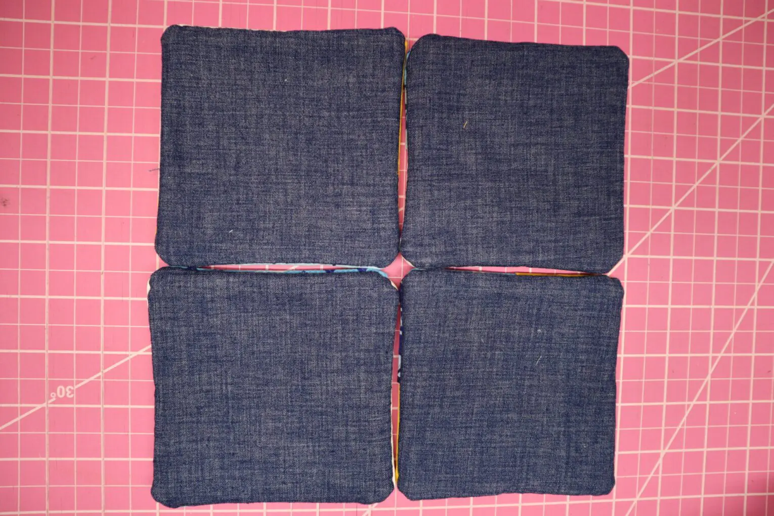 Four denim coasters arranged on a pink surface.