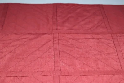 Red fabric with stitched geometric patterns and creases.