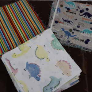 Colorful dinosaur-patterned cloths and striped fabric on a surface.